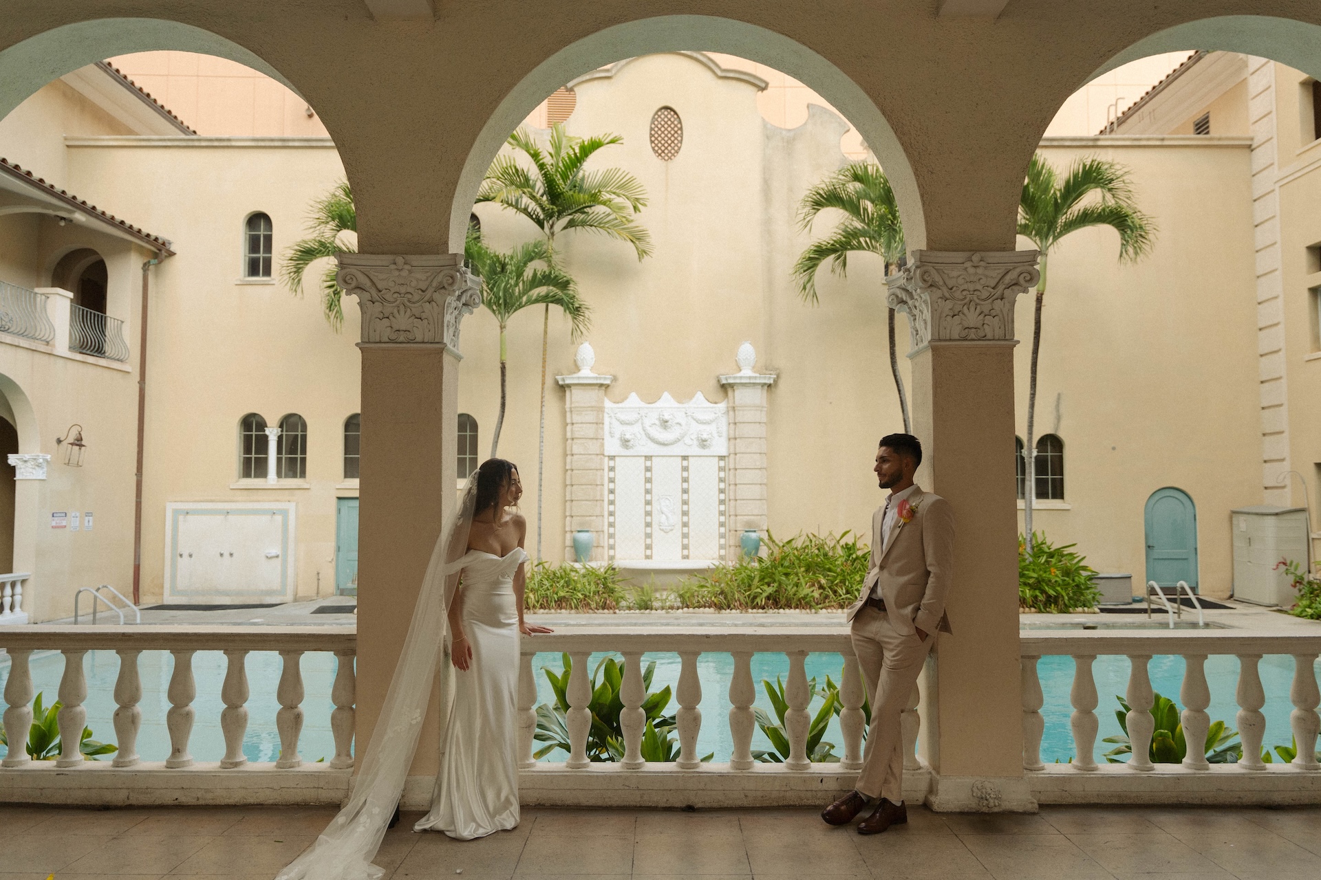 Bride and groom standing under arched columns near a pool – destination wedding in Hawaii setting.

