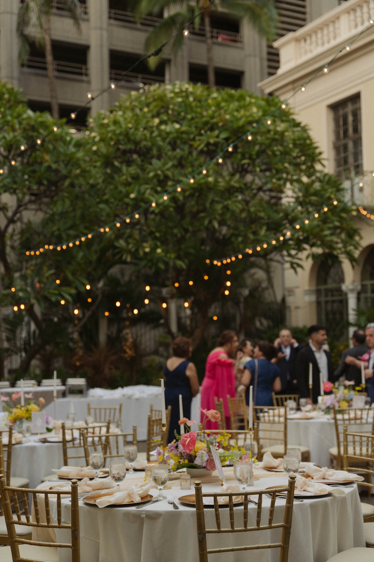 A wide shot of the reception tables set under twinkle lights, with floral centerpieces and gold chairs at the couple’s destination wedding in Hawaii.

