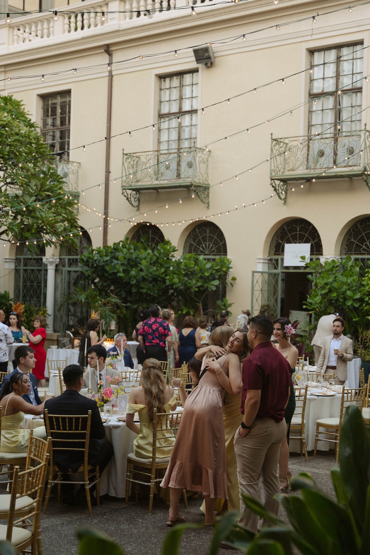 Guests mingle and hug under string lights in a courtyard reception space during a joyful destination wedding in Hawaii.

