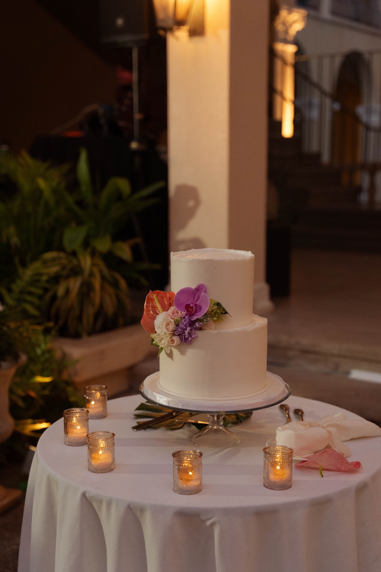 Close-up of the simple white two-tier wedding cake adorned with vibrant florals and surrounded by small votive candles.

