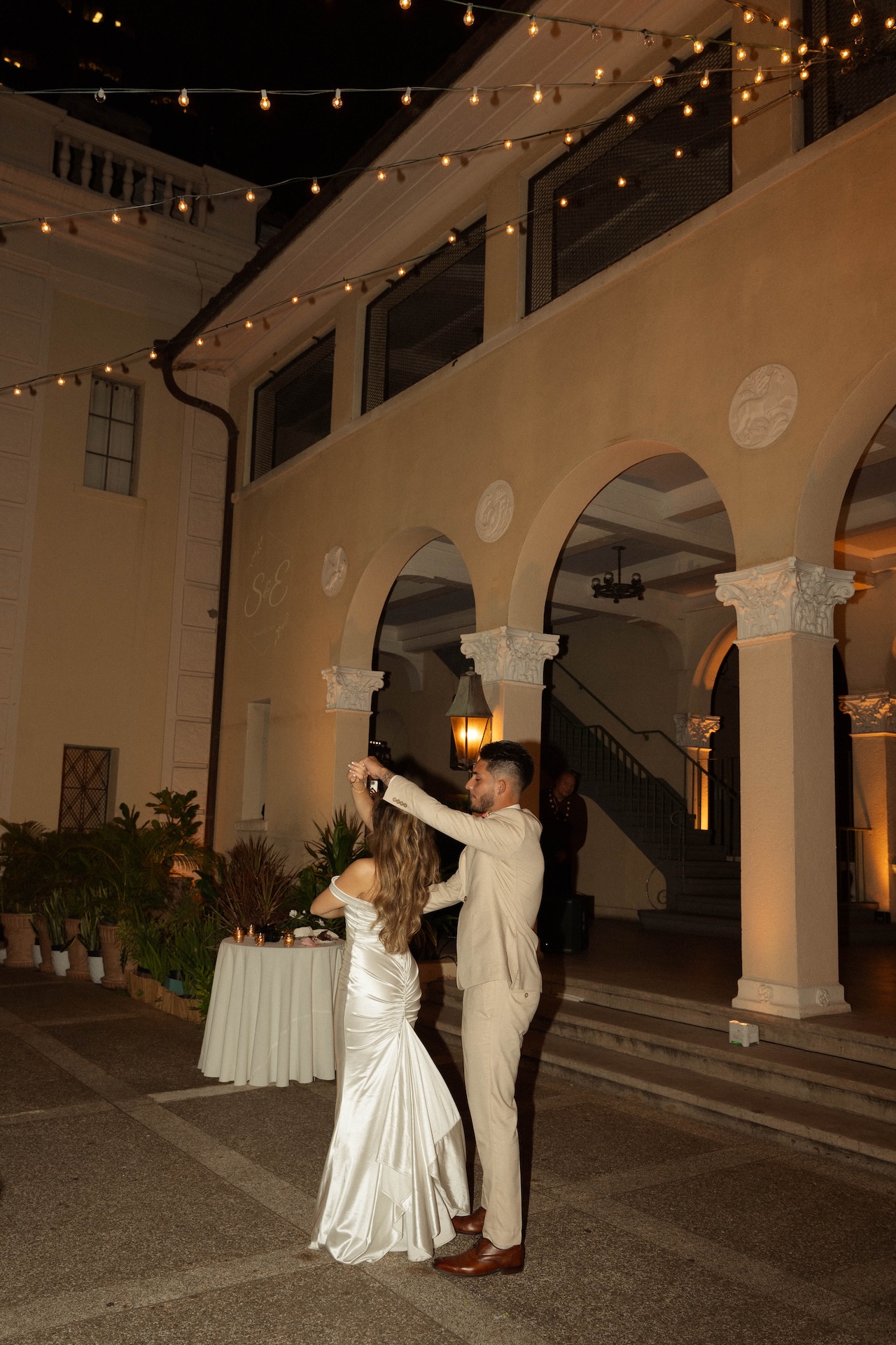 The groom twirling the bride around on the dance floor for their first dance under twinkling lights at their destination wedding in Hawaii
