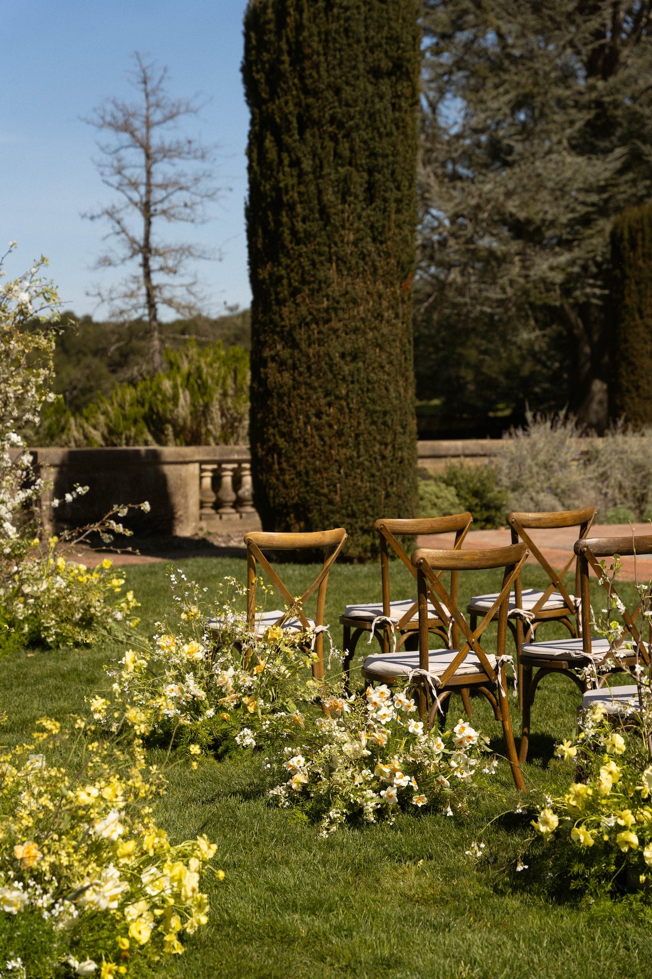 Wooden ceremony chairs arranged on a lush green lawn, surrounded by yellow and white floral arrangements at one of the most picturesque wedding estate venues.

