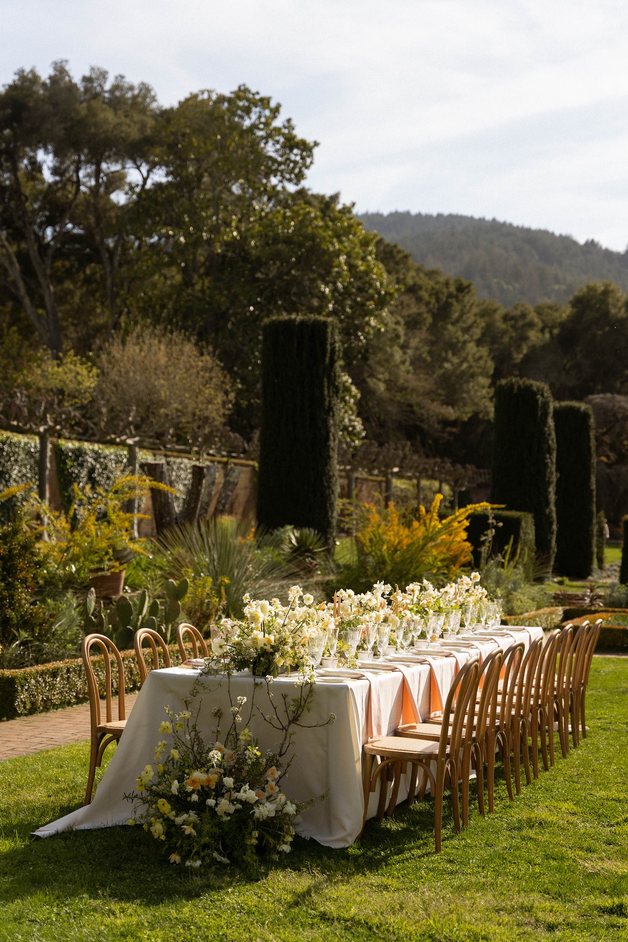 An outdoor reception table lined with wooden chairs and adorned with lush floral arrangements at one of the most timeless wedding estate venues.

