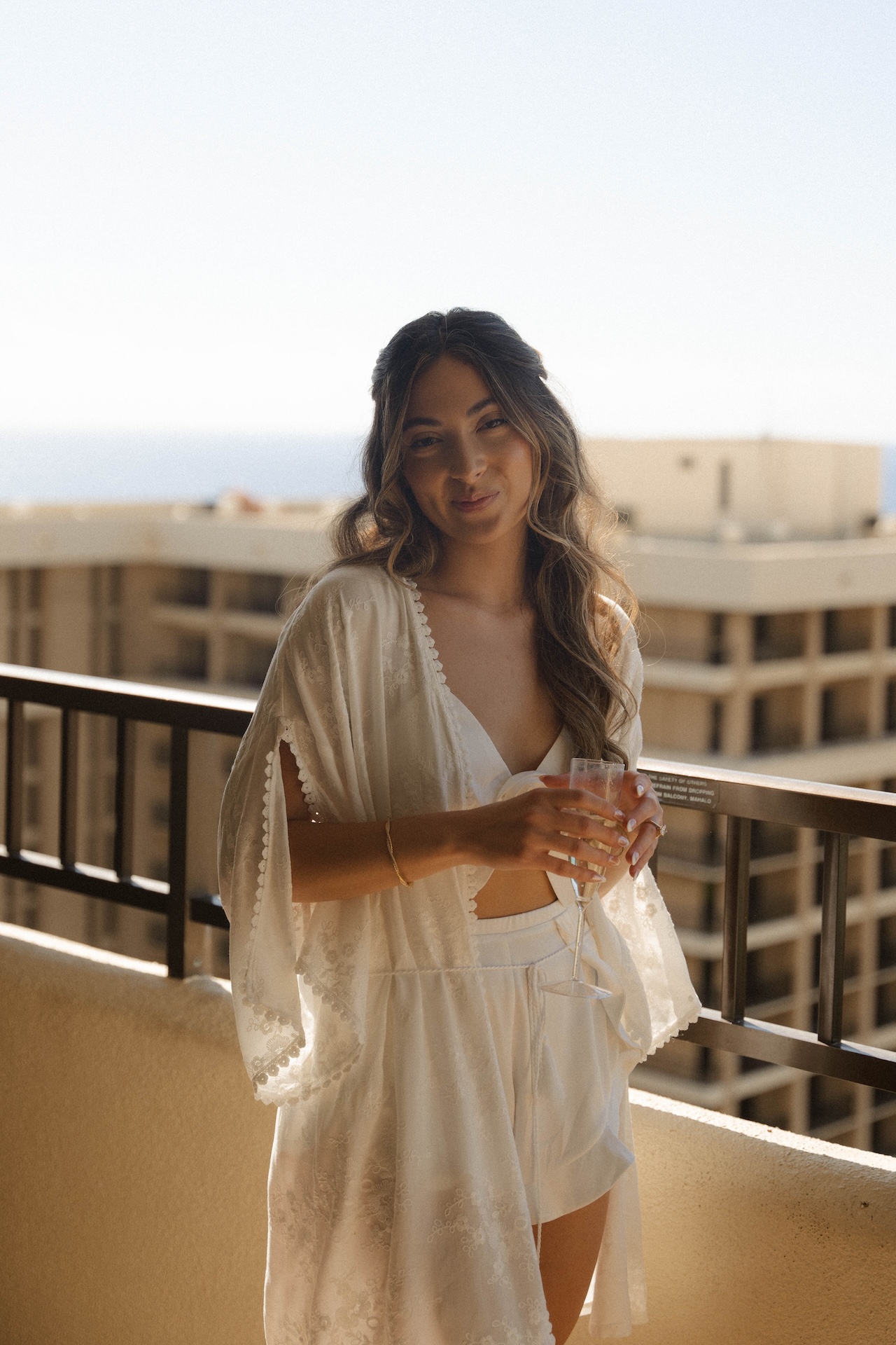 Bride sipping champagne on a balcony with ocean views in the background — destination wedding in Hawaii feel.

