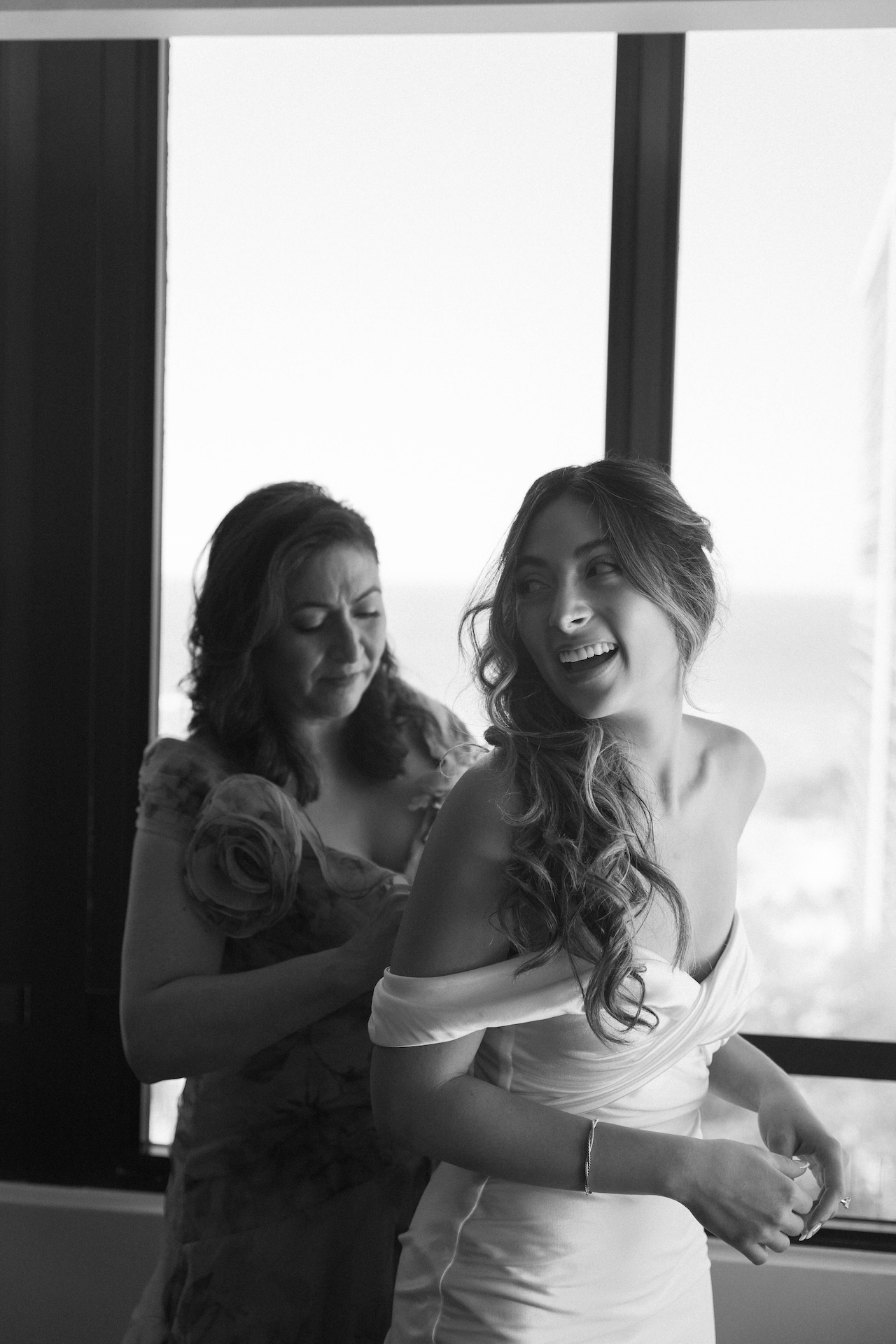 Mother helping the bride into her dress while they both smile.


