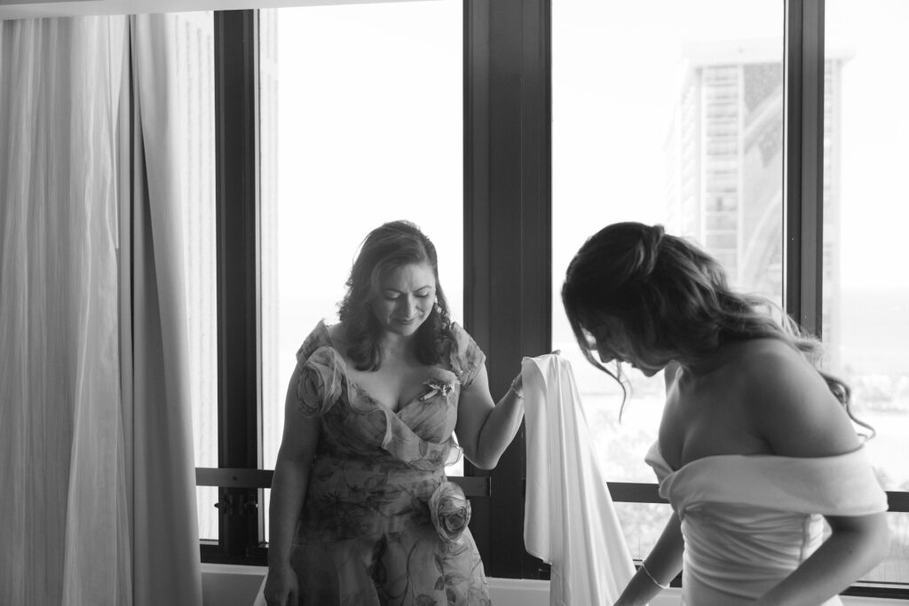 Bride getting ready with help from her mother near a bright window.

