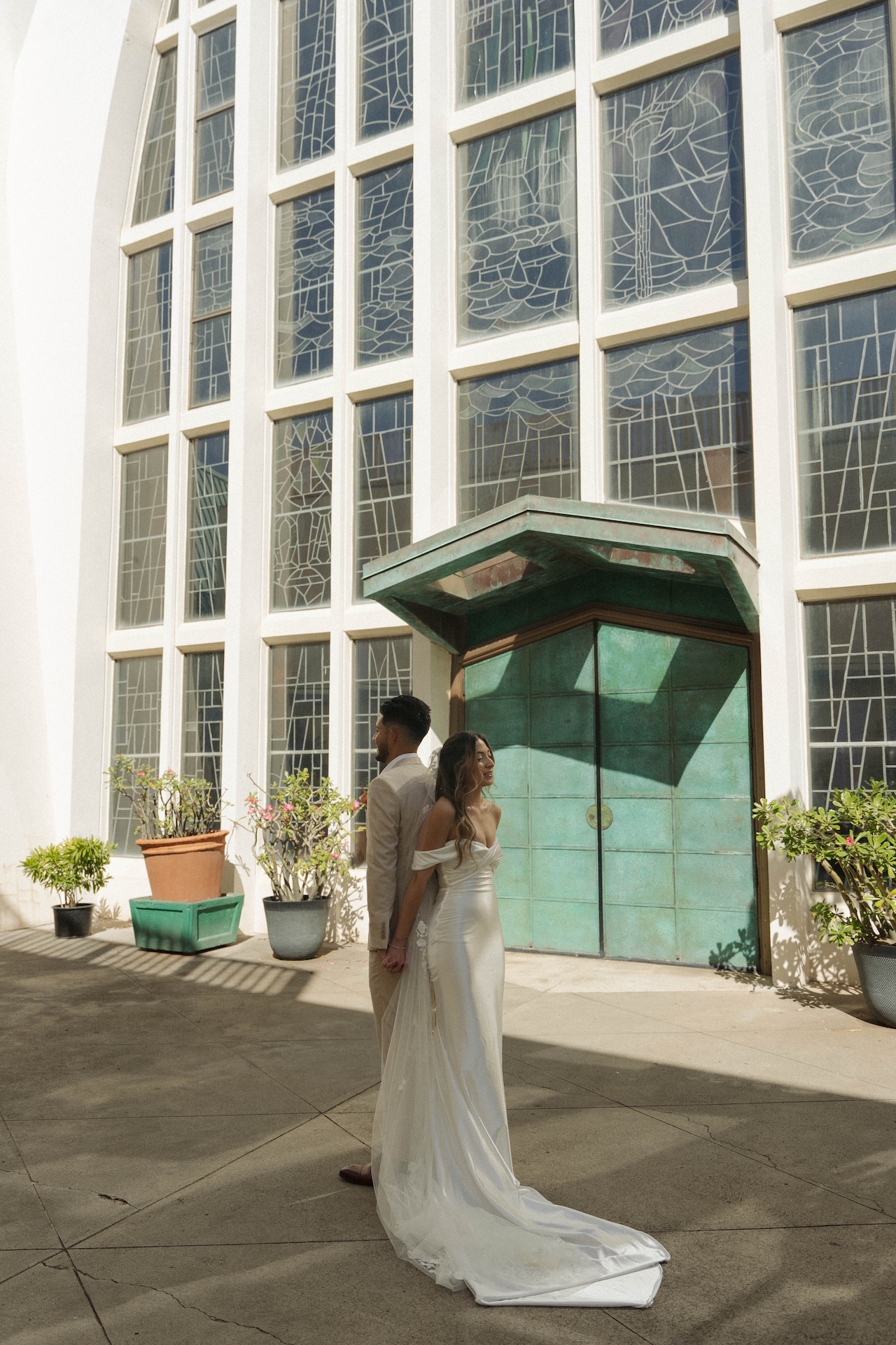 Bride and groom standing outside a church with stained glass windows, holding hands before their first look.

