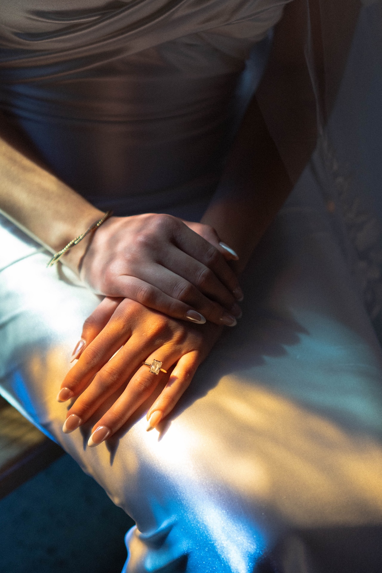 Close-up of the bride’s hands resting on her satin dress, featuring her engagement ring.

