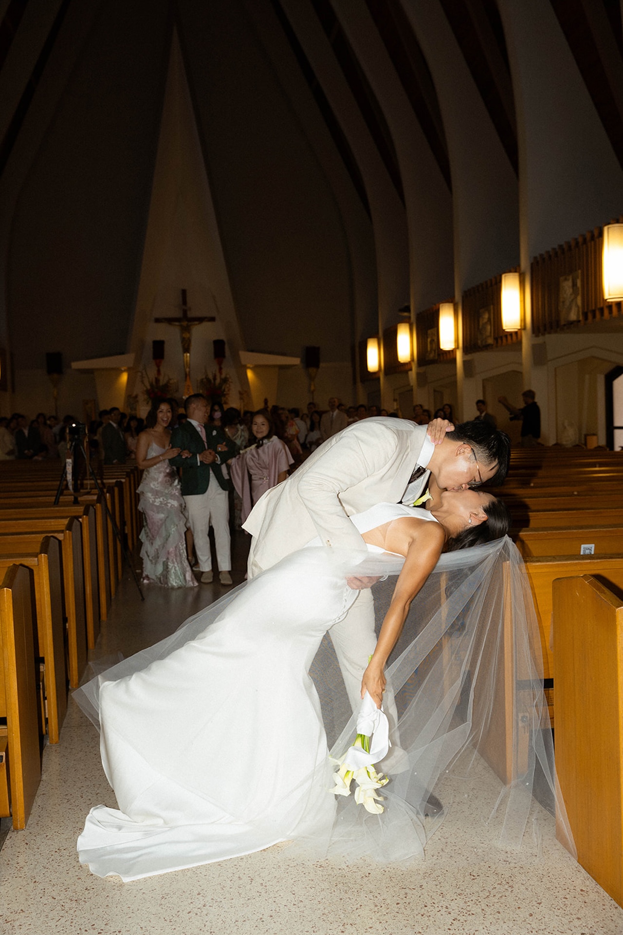 Groom dipping the bride for a kiss in the center aisle of the church, her veil flowing behind them in a dramatic moment