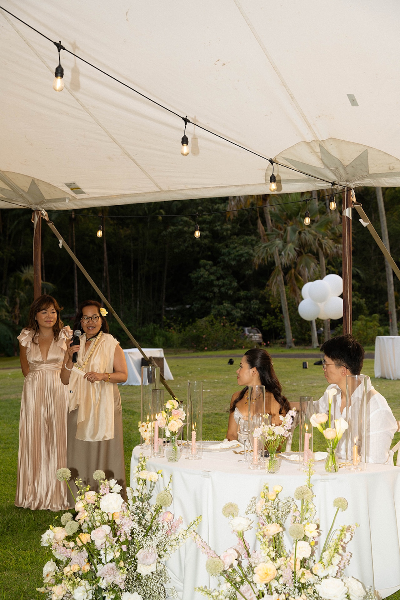 A heartfelt toast under a sailcloth tent, surrounded by floral centerpieces and string lights — an evening celebration at one of Hawaii’s most intimate wedding venues