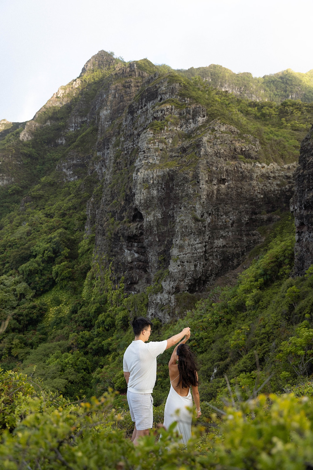 Bride twirling on a mountaintop in a sleek white dress while the groom watches – a breathtaking elopement-style shoot inspired by Hawaii’s hidden landscapes and intimate wedding venues