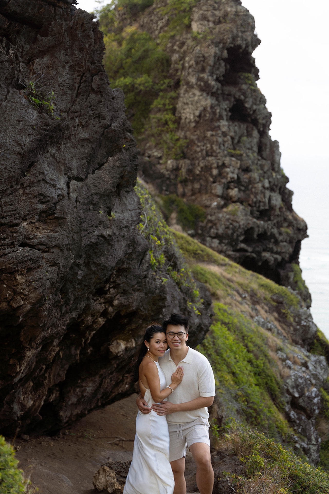 Couple embracing in front of dramatic cliffside views, with the ocean just barely visible through the rocks – perfect inspiration for couples seeking adventure-filled intimate wedding venues in Hawaii