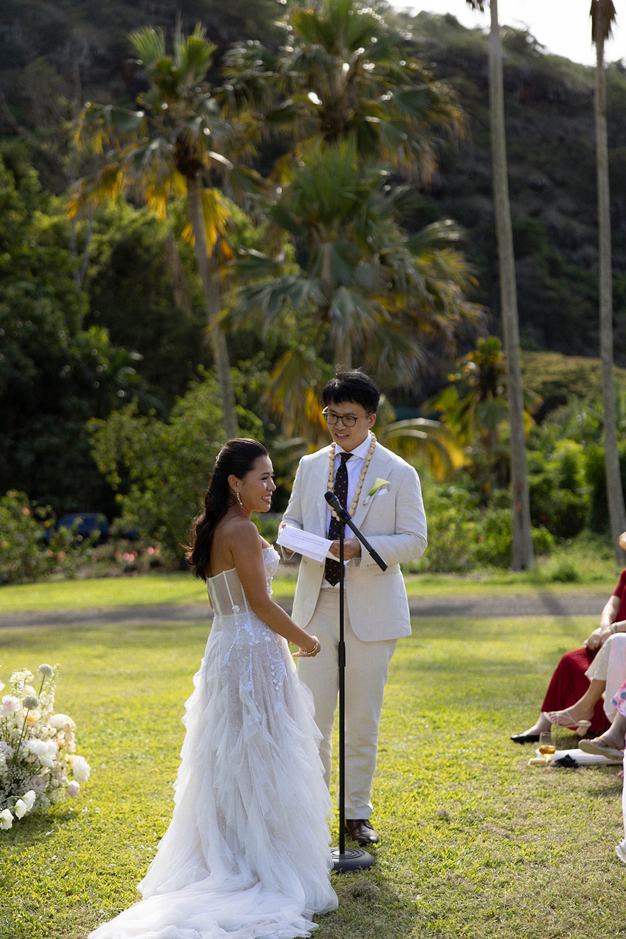 Groom reading vows as the bride laughs during their outdoor ceremony, surrounded by palm trees and golden light