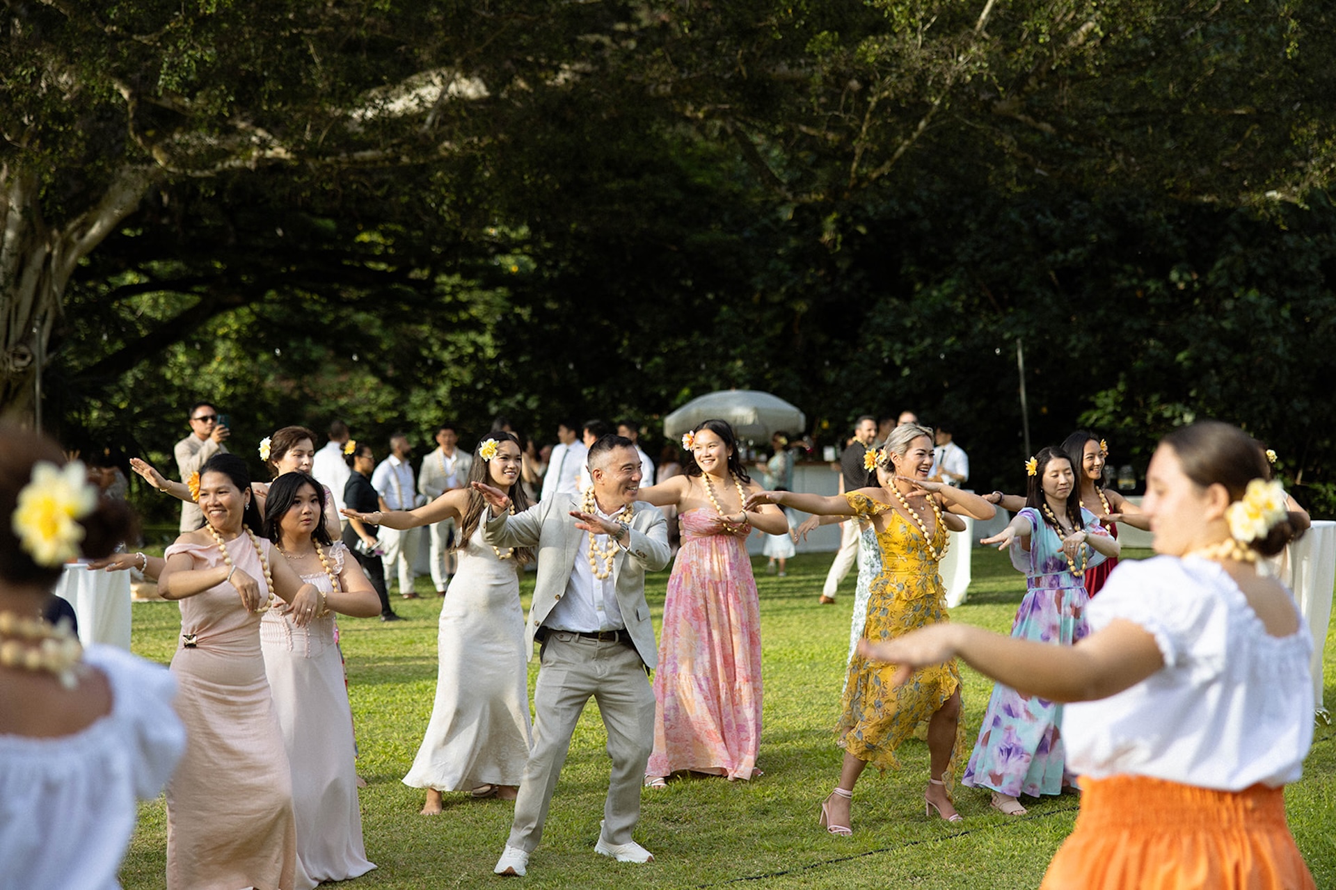 Family and friends performing a traditional hula dance on the grass, celebrating with music and movement at a tropical outdoor reception — this is the kind of culture-filled energy that makes intimate wedding venues in Hawaii so unforgettable