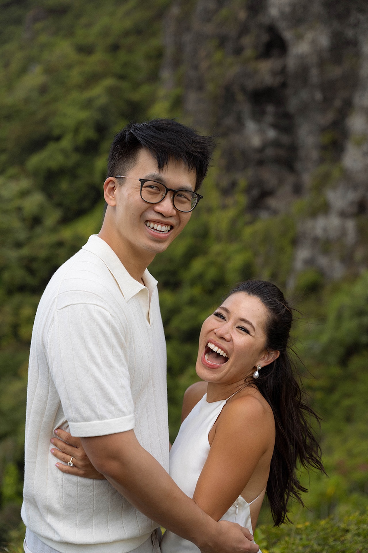 Couple laughing in each other’s arms, surrounded by cliffs and greenery during their mountaintop session