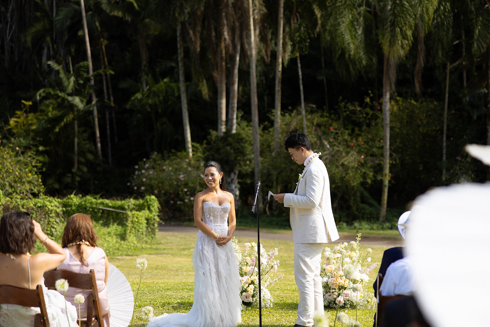 Bride and groom exchanging vows outdoors in a private ceremony, with palm trees and soft florals creating a serene jungle backdrop
