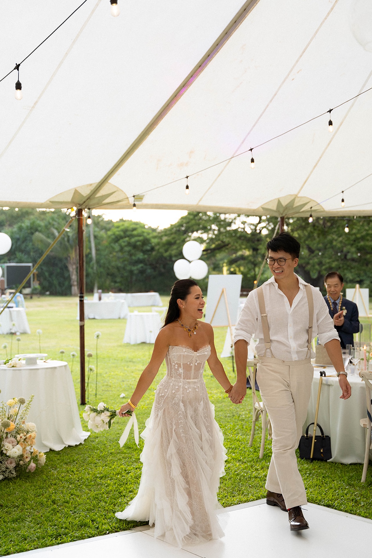 Bride and groom entering the tent hand-in-hand with huge smiles, ready for their reception entrance