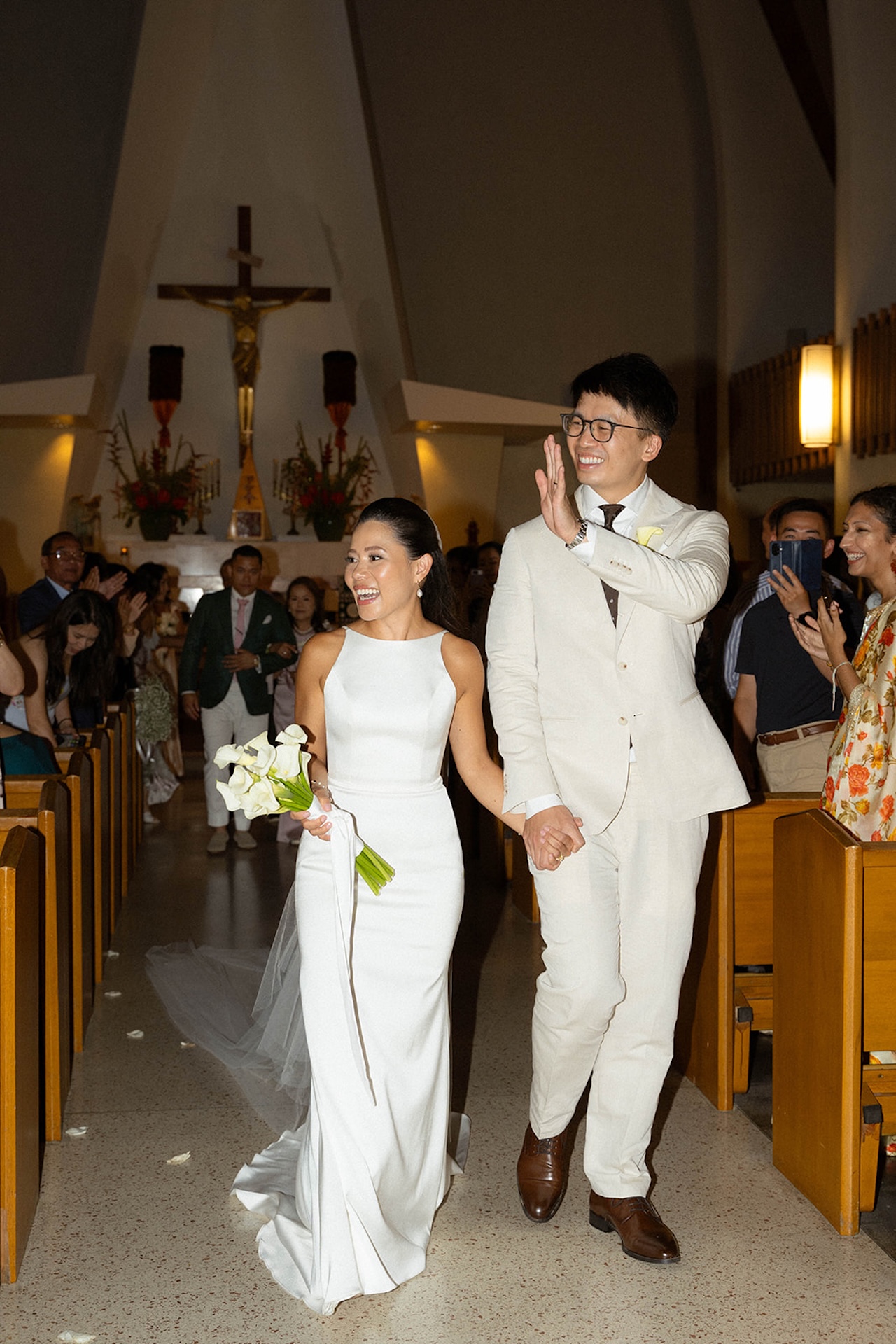 Bride and groom walking down the church aisle hand-in-hand after their ceremony, smiling and waving — a joyful moment in one of Oahu’s most timeless and intimate wedding venues