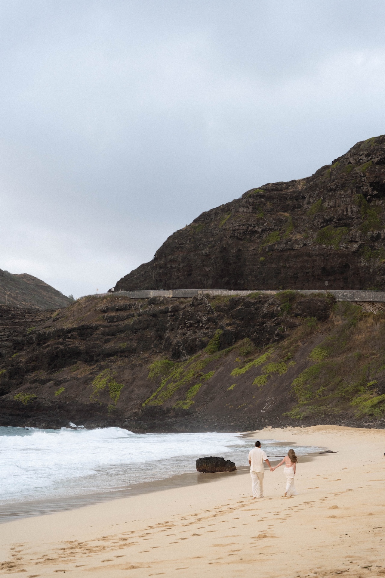 Pair walking hand in hand into the distance during their beach proposal, footprints trailing in the sand behind them.