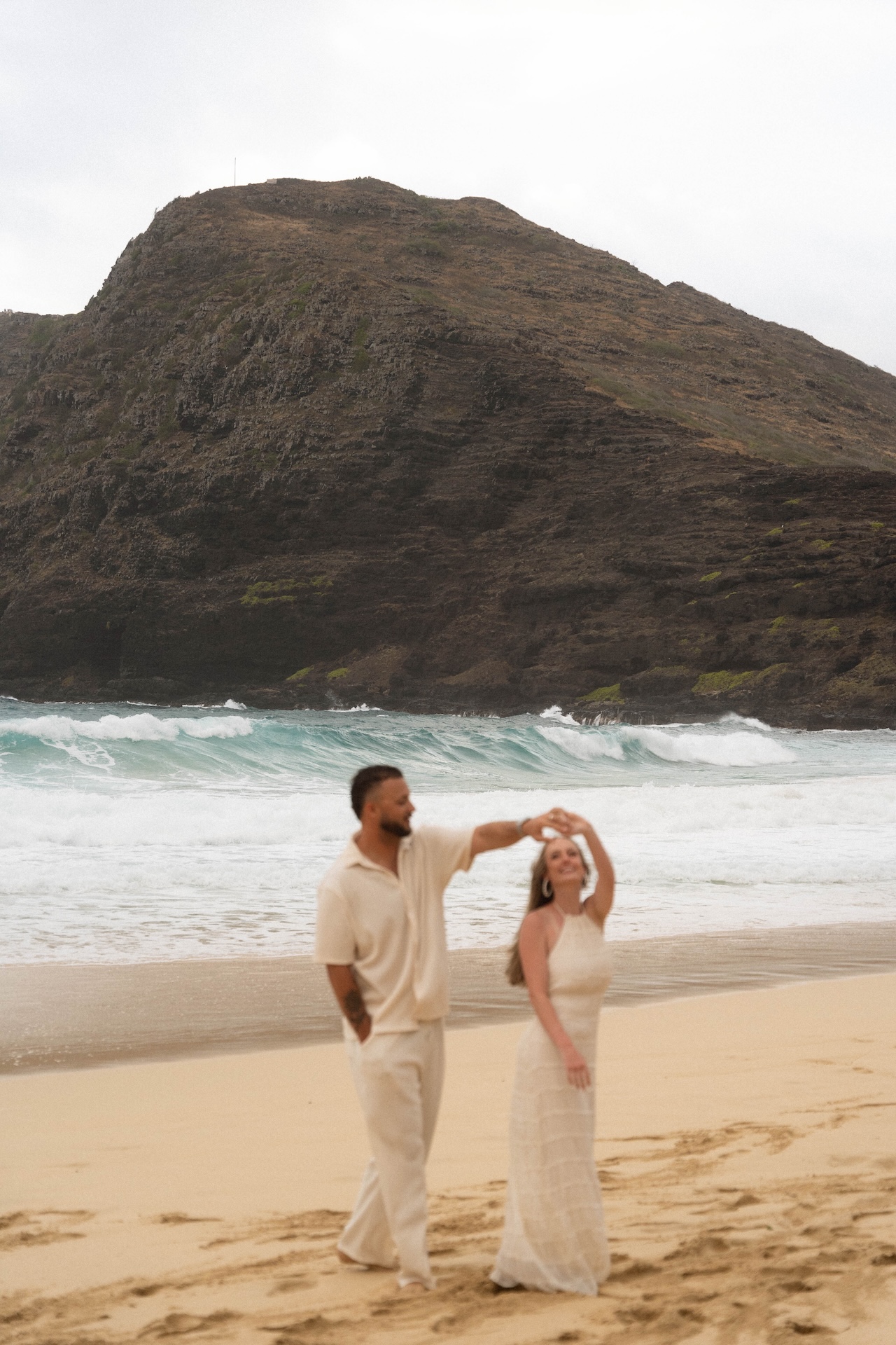 Playful beach proposal moment as the couple dances on the shoreline, twirling against the backdrop of crashing waves.