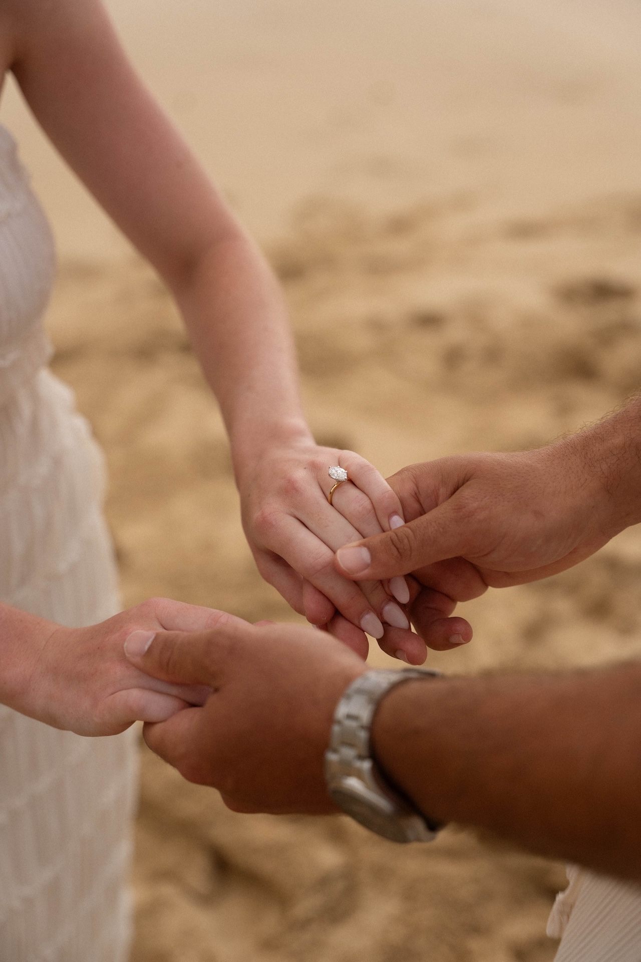Close-up of the couple’s hands intertwined, highlighting the engagement ring as they stand barefoot in the sand.
