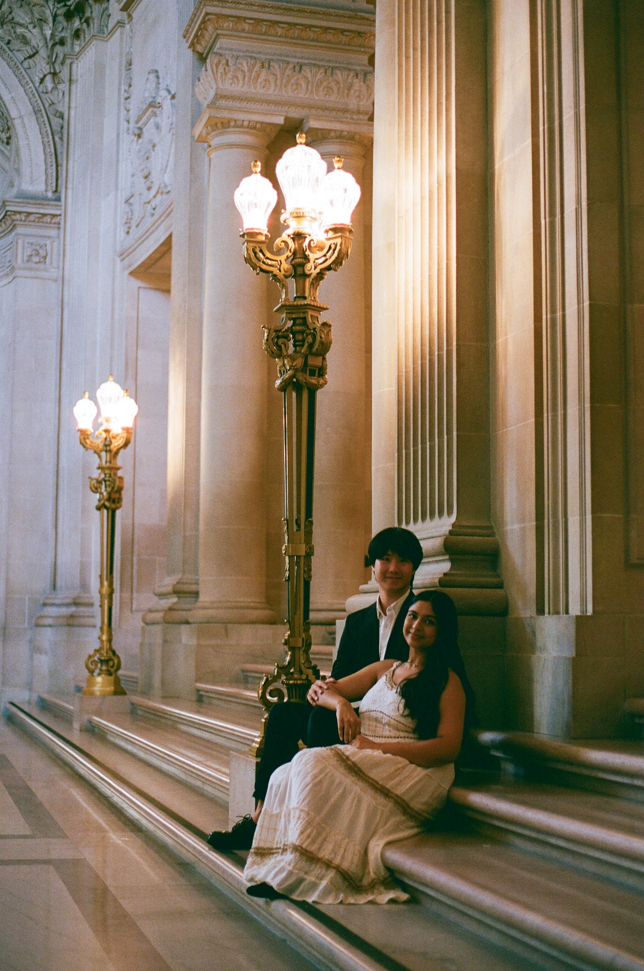 The bride leaning against the groom while they sit on the staircase at the San Francisco City Hall after their wedding.