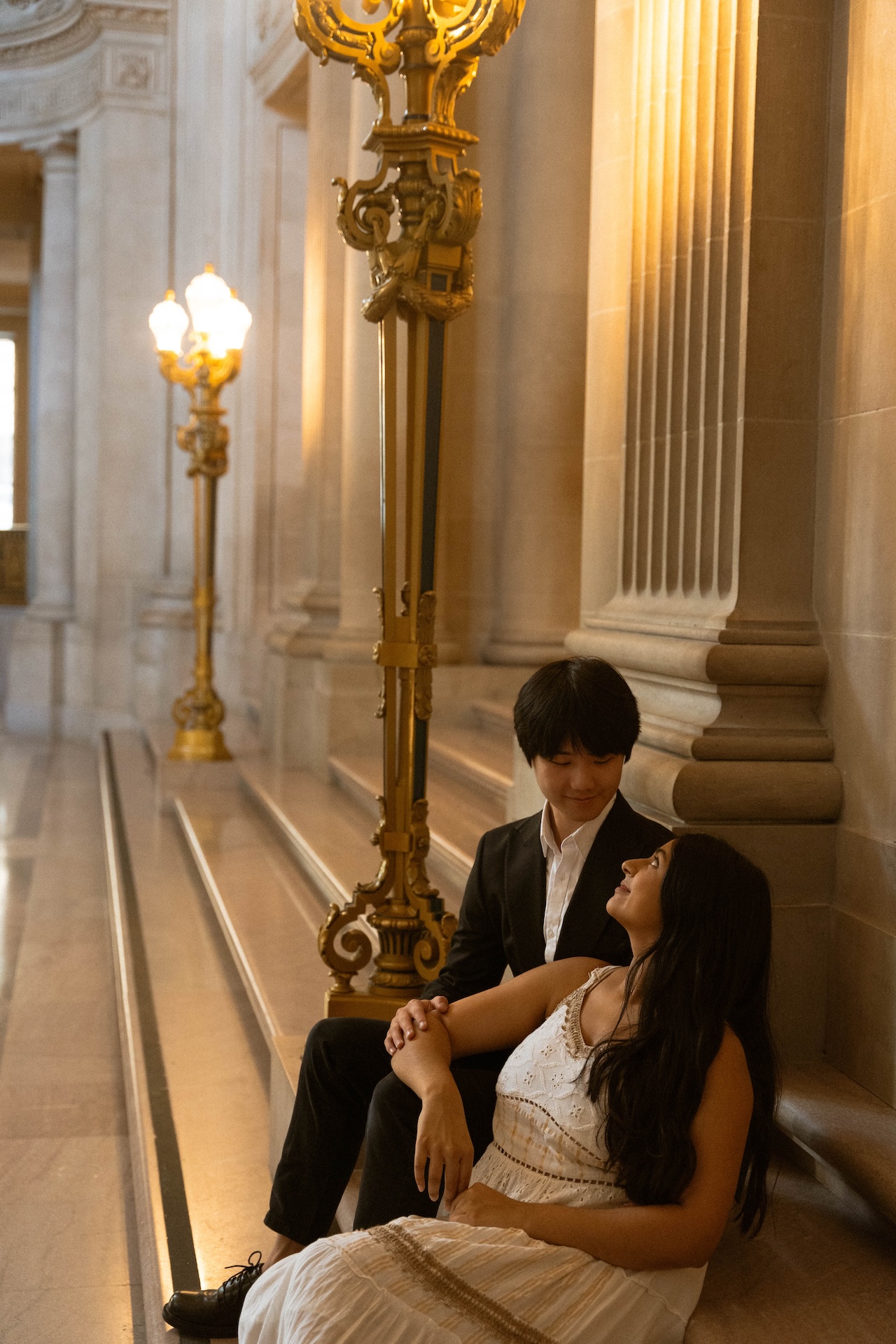 The bride leaning against the groom while they sit on the staircase at the San Francisco City Hall after their wedding.
