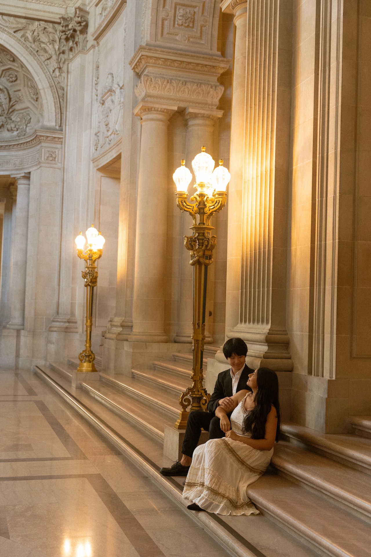 The bride leaning against the groom while they sit on the staircase at the San Francisco City Hall after their wedding.