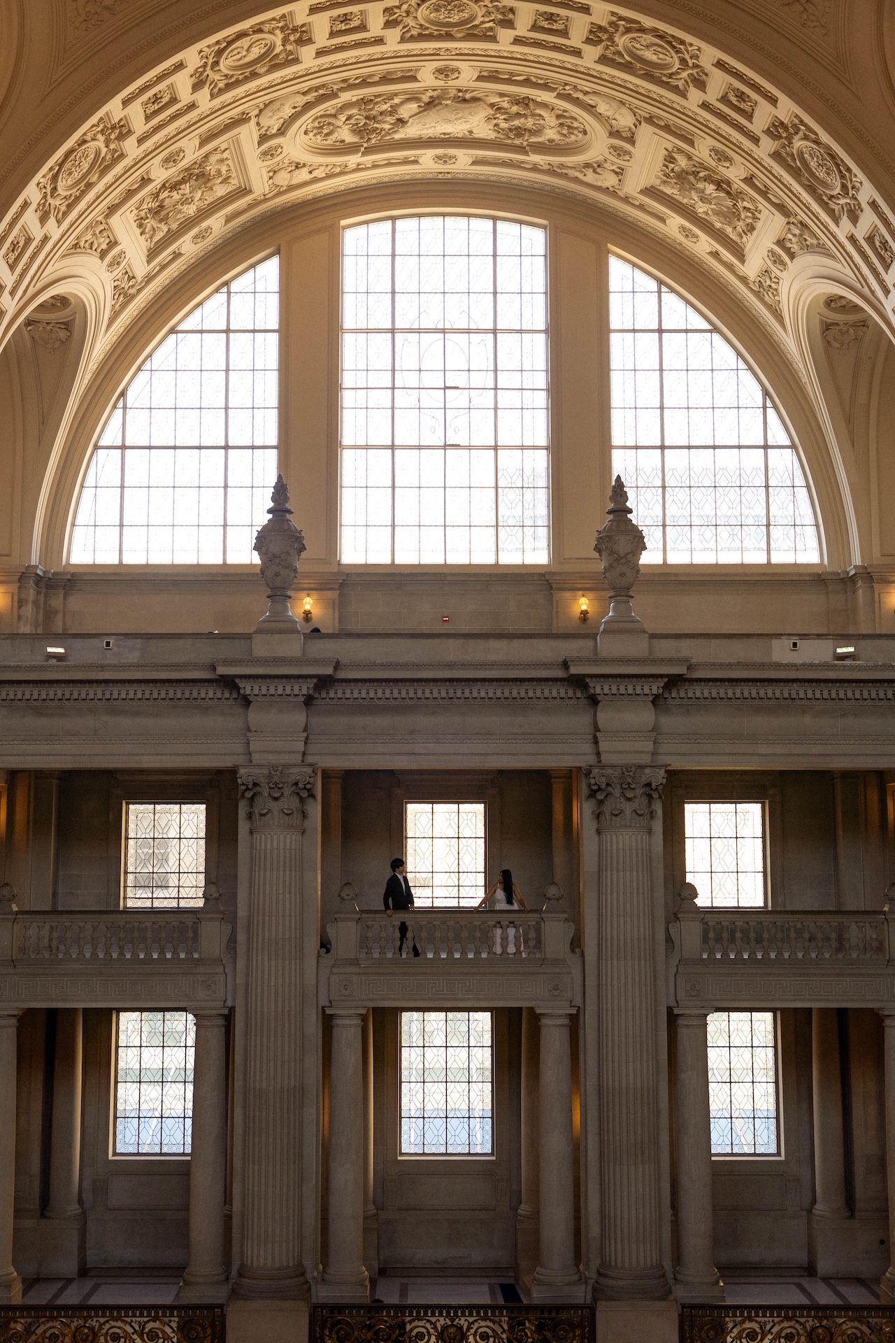 The bride and groom leaning over the balcony on the 3rd floor of the San Francisco City Hall