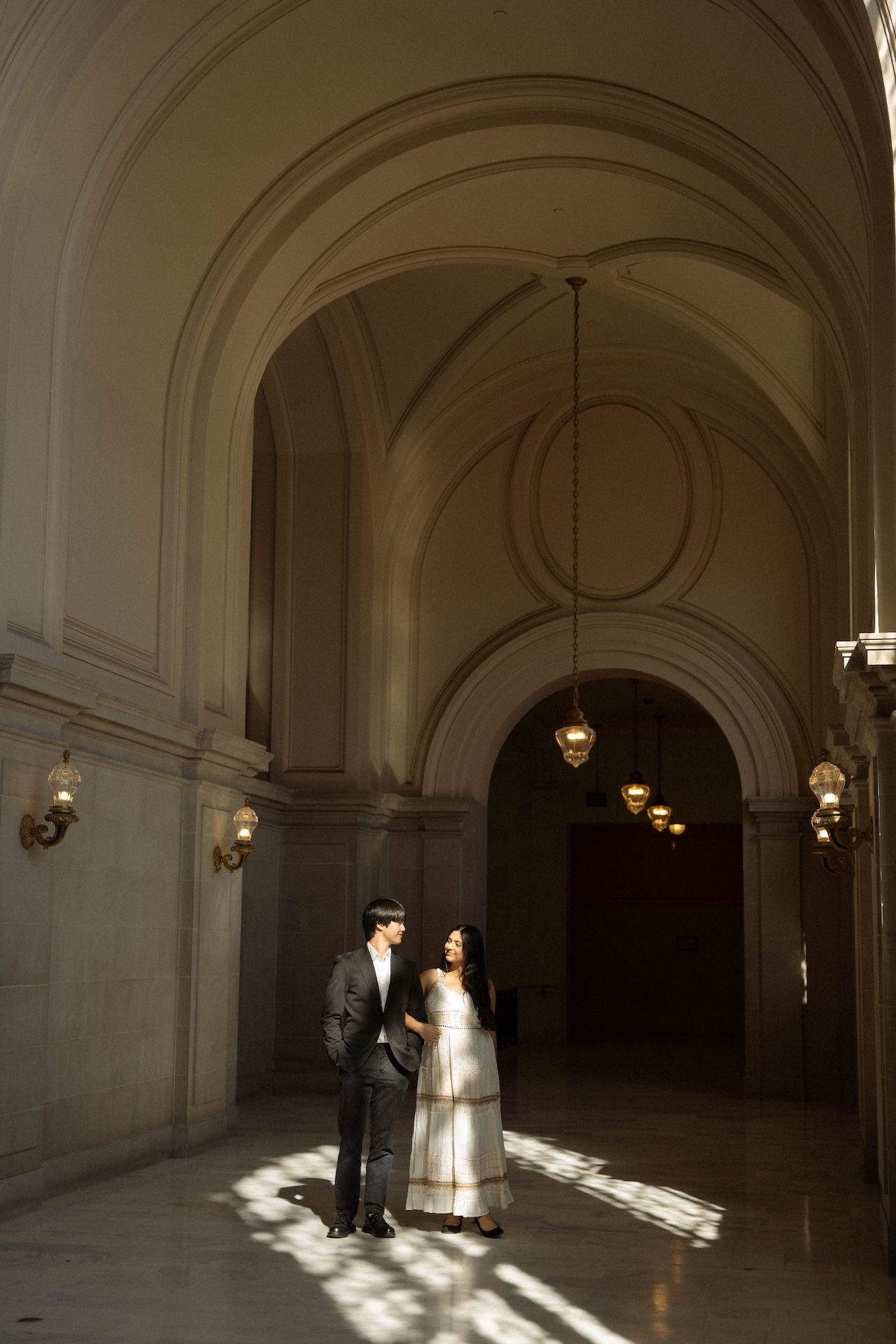 A couple walking down a long, arched hallway, bathed in natural light. This is a classic shot from a San Francisco City Hall wedding.