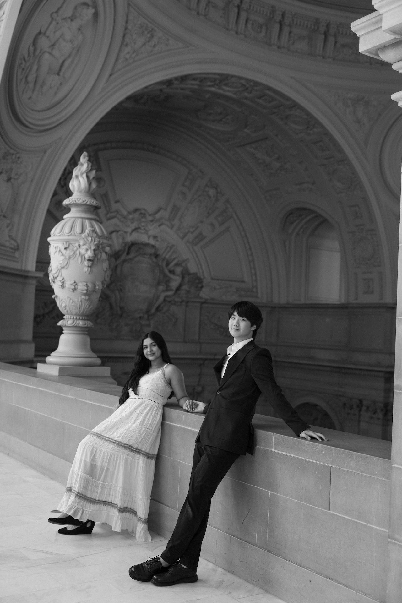 A black and white photo of a bride and groom leaning against the railing of the rotunda room at the San Francisco City Hal