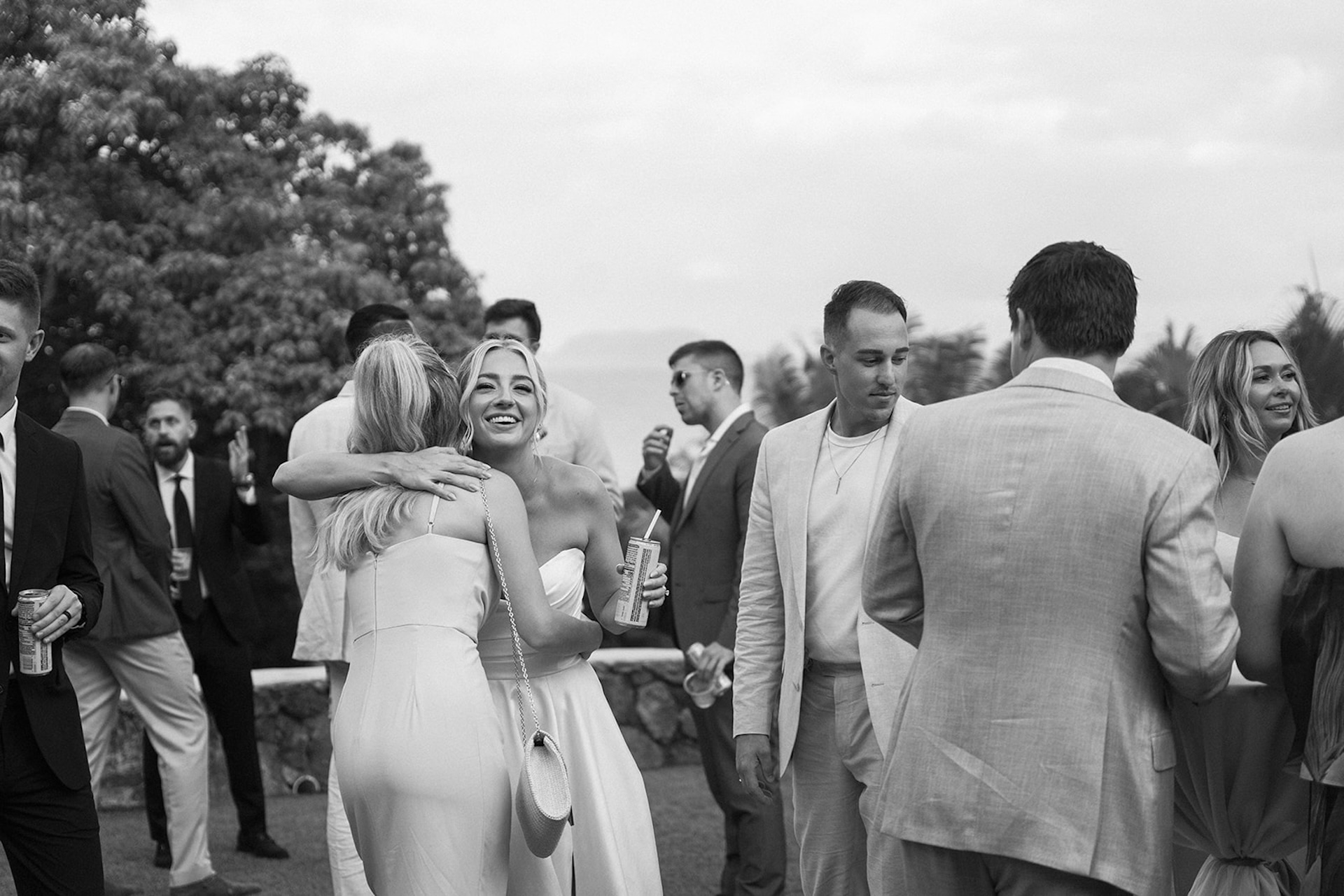 The bride hugs a guest during cocktail hour, smiling joyfully while guests mingle in the background.