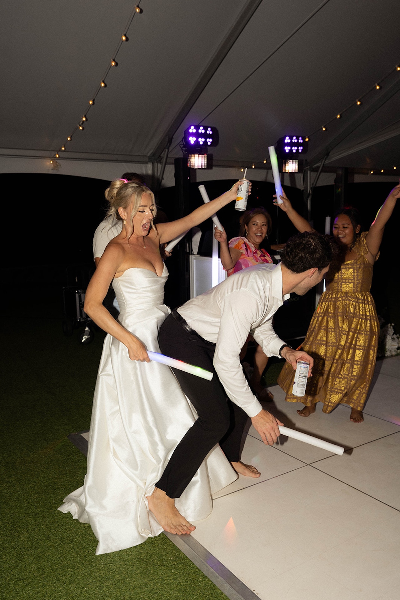 Bride and groom dancing barefoot with glow sticks, surrounded by laughing guests – fun Hawaii wedding planning moment.