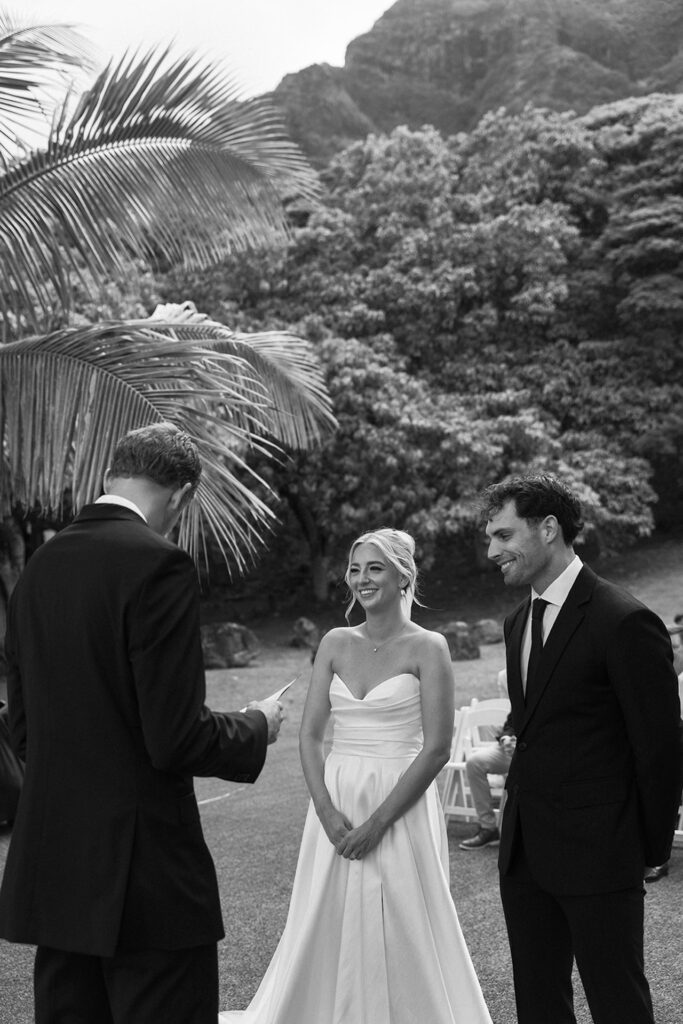 Smiling during the ceremony, the couple listens to their officiant—a joyful moment during their Hawaii wedding planning celebration.