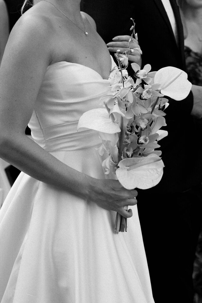 A close-up of the bride holding her modern white orchid bouquet, with elegant tropical details.