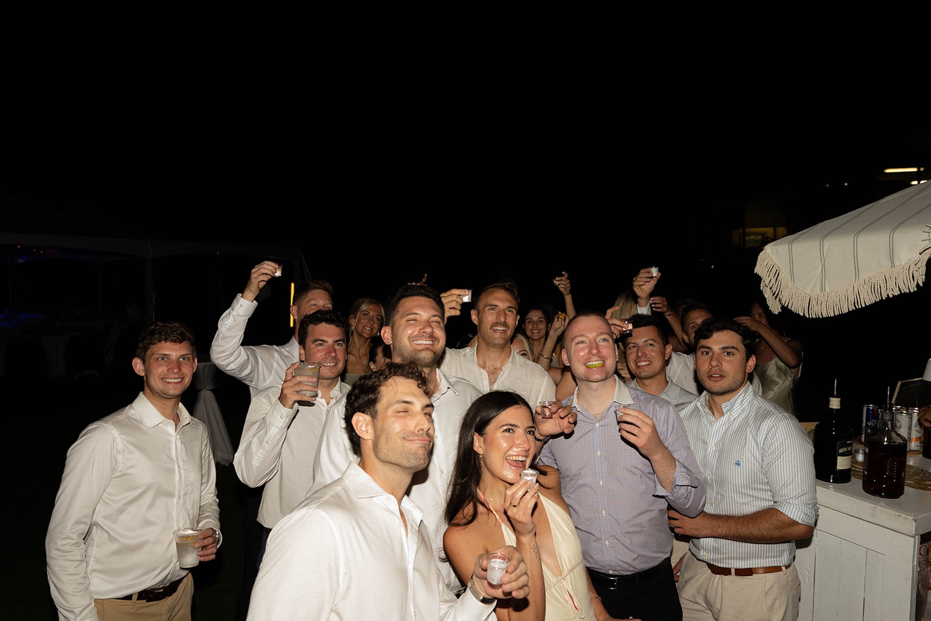 Flash photo of the groomsmen and wedding guests smiling, laughing and cheersing during the reception.