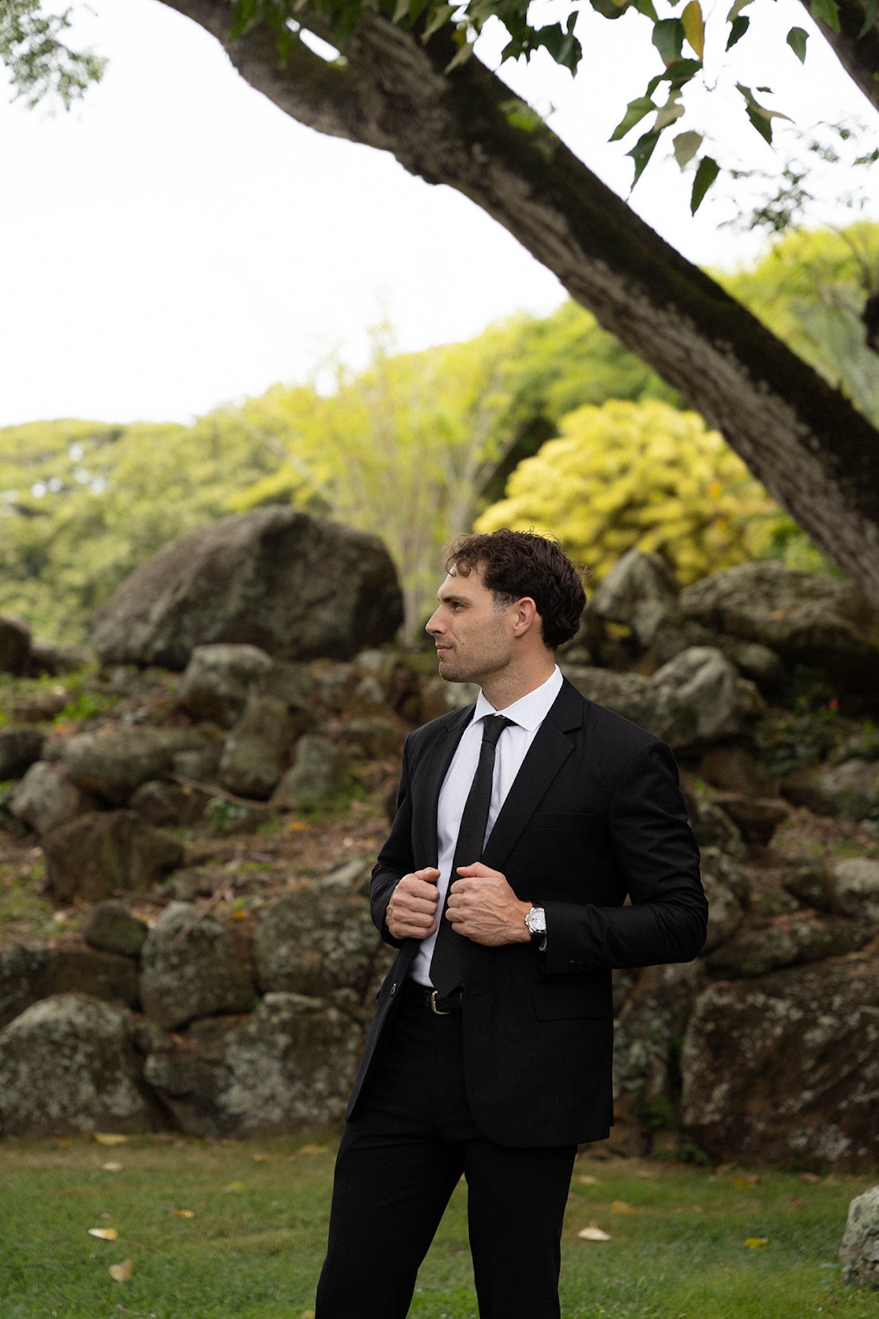 Groom adjusting his suit jacket in a quiet tropical garden, preparing for the ceremony.