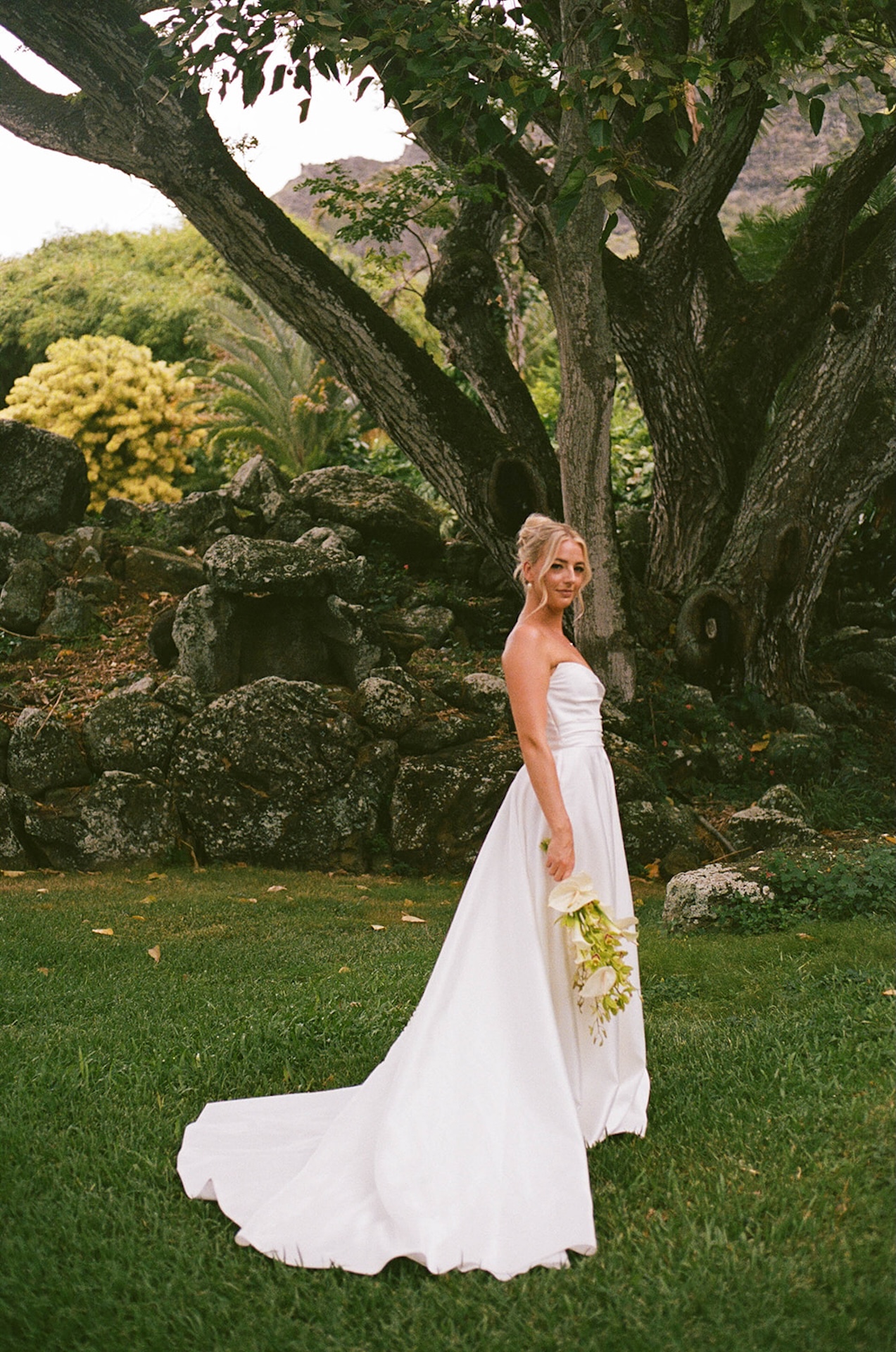 Stunning shot of the bride holding her orchid bouquet during bridal portaits with lava rocks and lush greenery behind her.