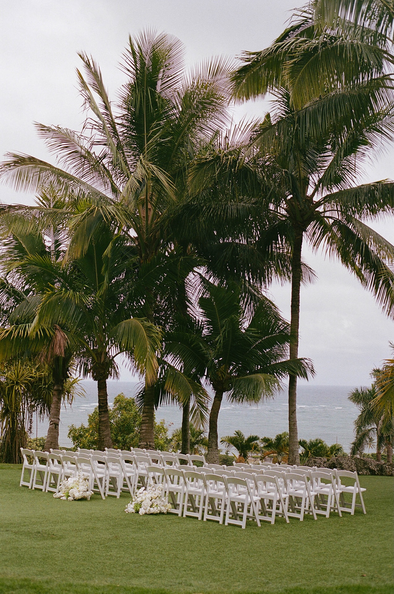 A stunning film detail photo of the wedding ceremony set up including chairs and elegant white florals while doing their Hawaii wedding planning.