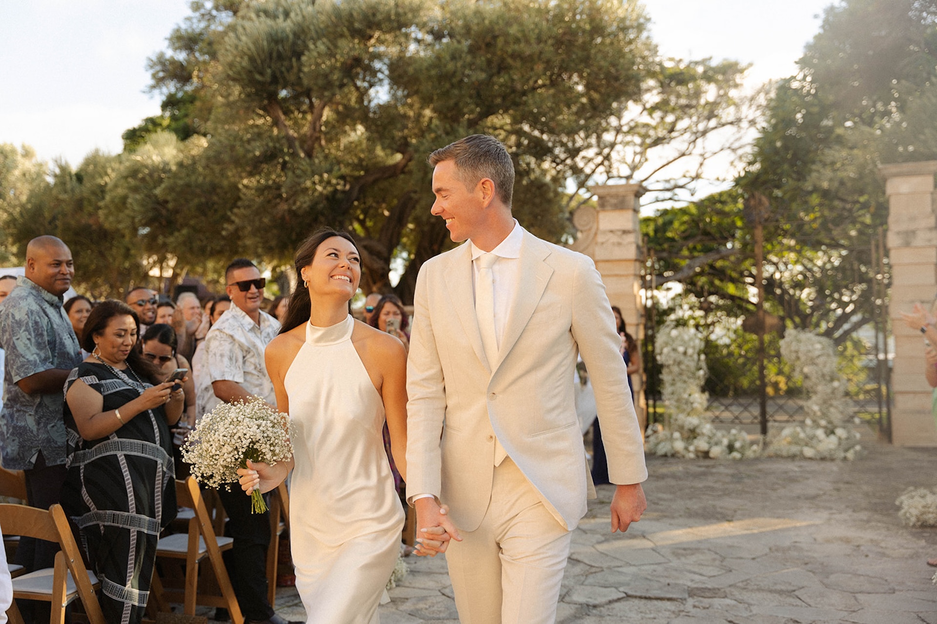 Newlyweds beam as they walk down the aisle surrounded by guests and tropical trees, the perfect glimpse into the best destination wedding locations.