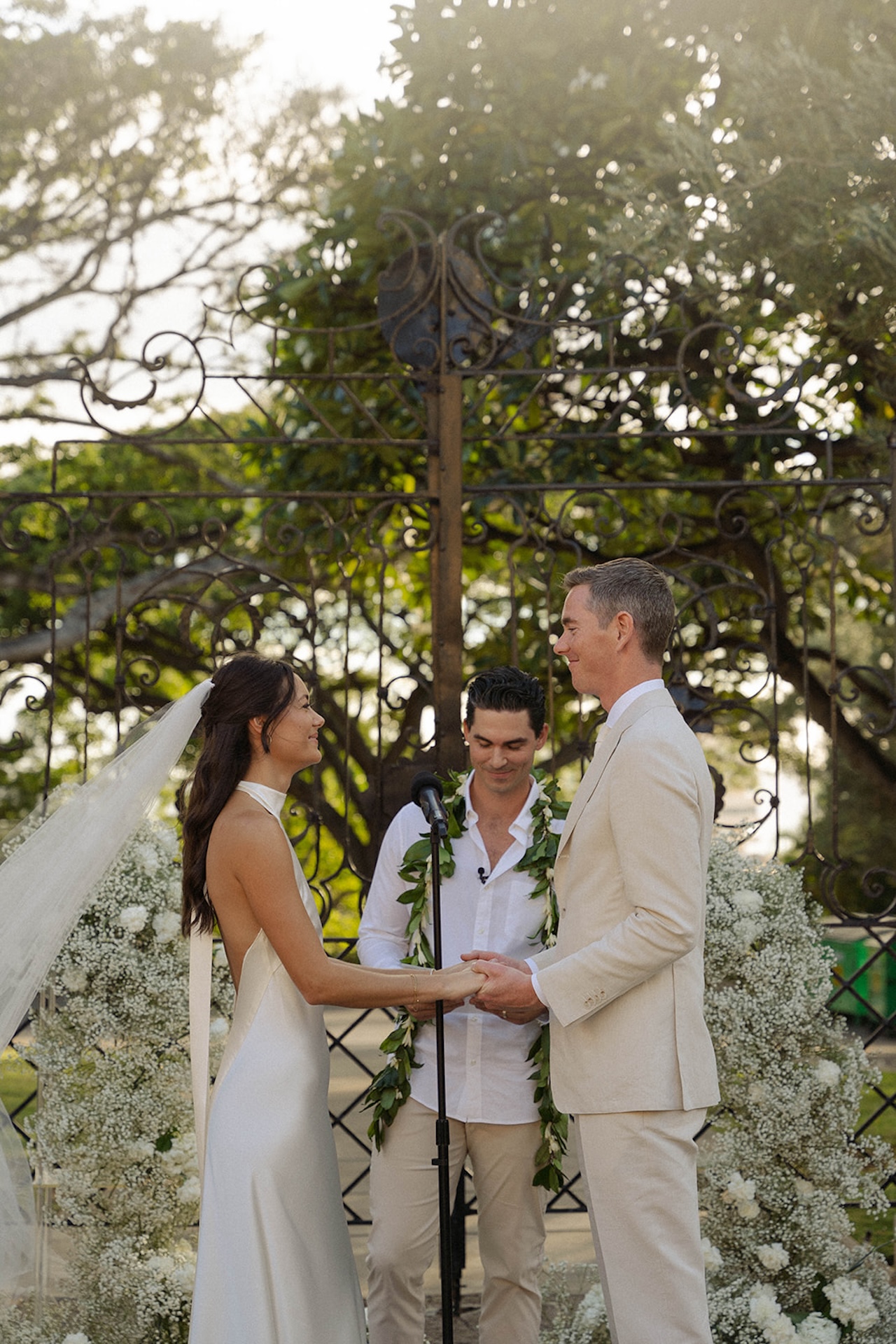 The bride and groom smiling holding hands at the alter with the sun shining through the trees behind them