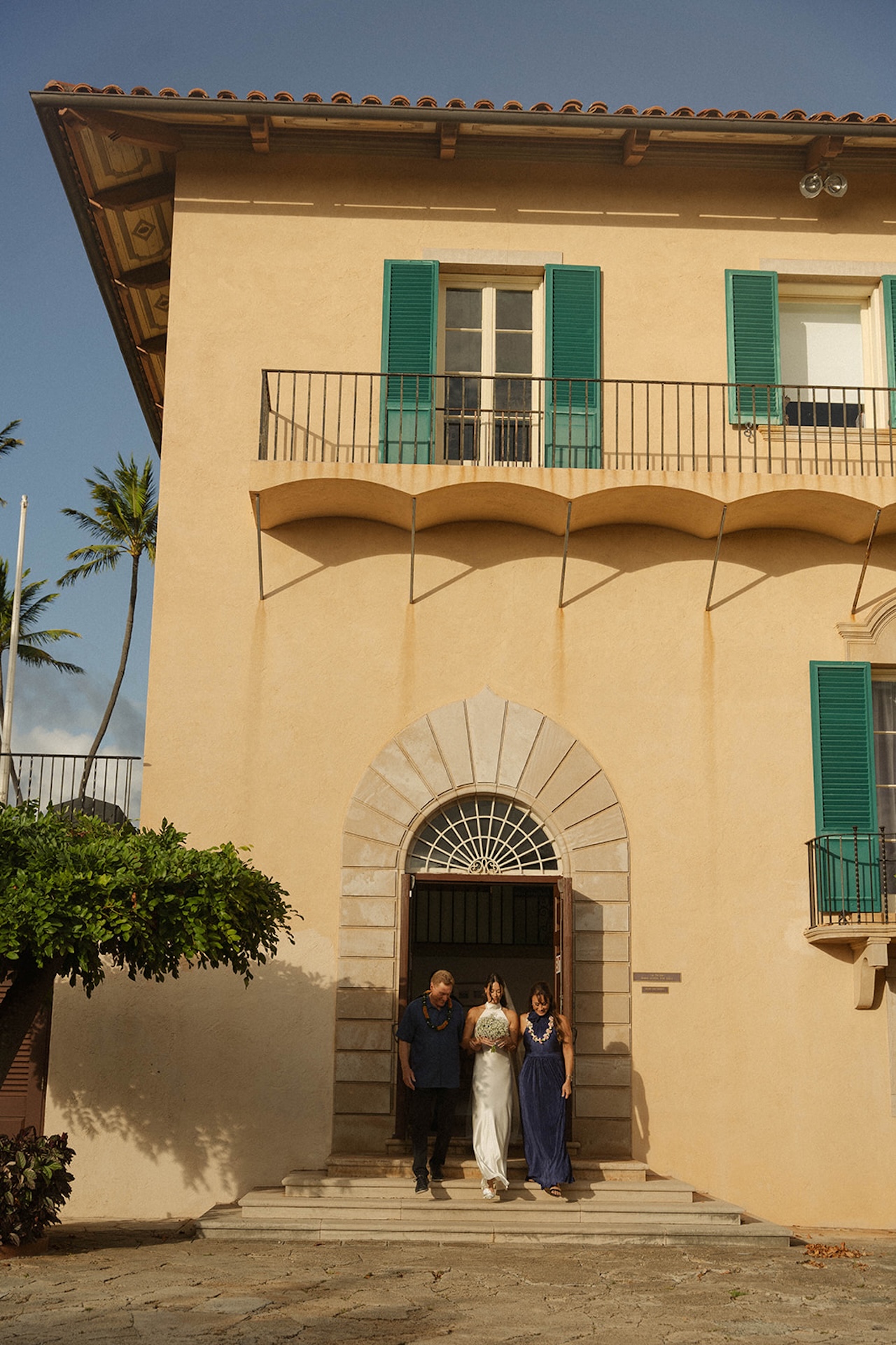 The bride walks down the steps of a historic villa, sunlight glowing around her — a breathtaking intimate wedding entrance.