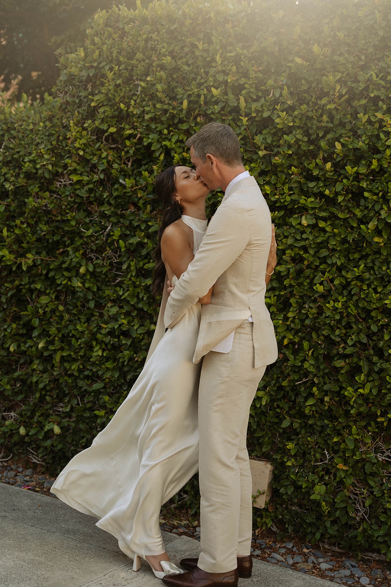 The couple shares a sweet kiss in the golden light beside lush greenery, showcasing effortless romance in one of the best destination wedding locations.