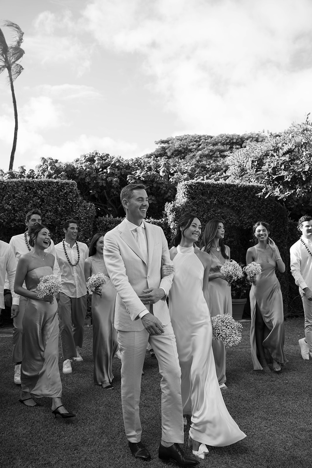 The couple walks through lush gardens with their wedding party laughing behind them — a joyful celebration at one of the best destination wedding locations.