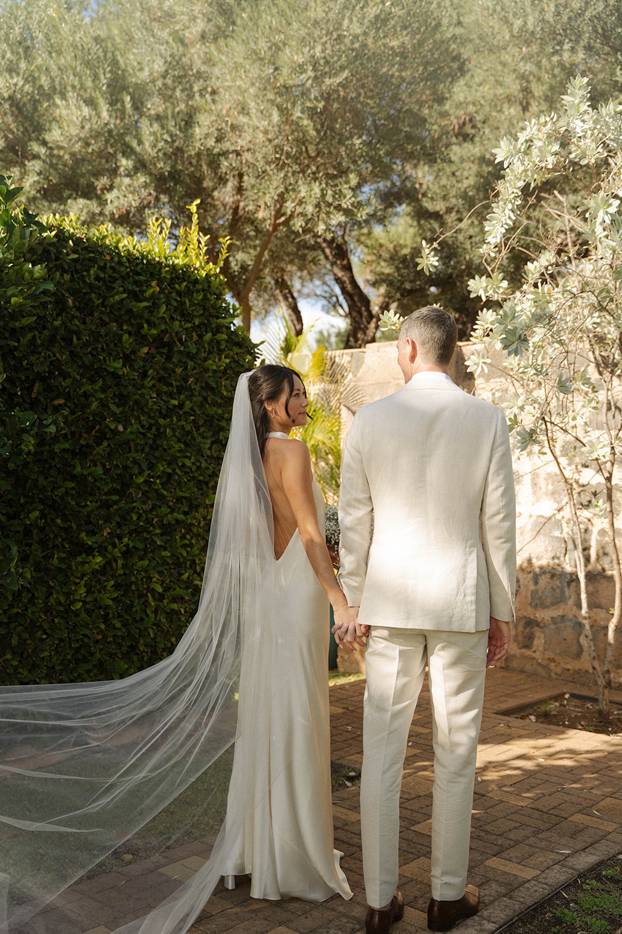 An elegant sunlit bride and groom portrait of the bride and groom standing and walking along the stone alley with her veil flowing in the wind during their intimate wedding.