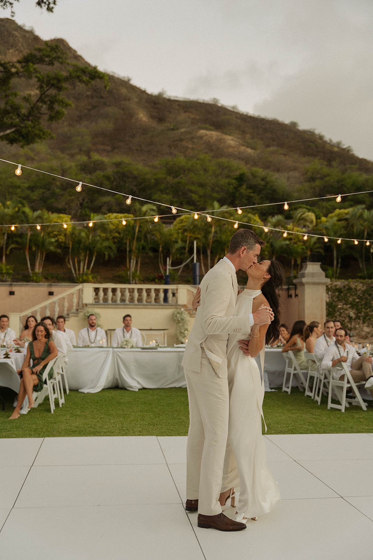 The couple shares a joyful first dance under warm string lights, surrounded by friends and family, representing the elegance of the best destination wedding locations.