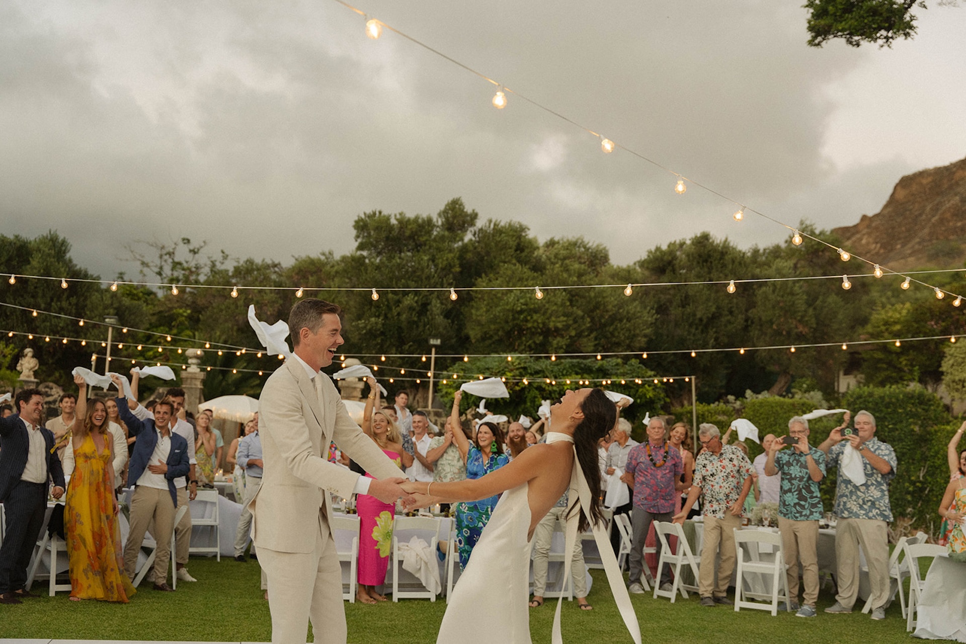 Guests cheer with napkins in the air as the couple laughs and dances together, an unforgettable intimate wedding reception moment.