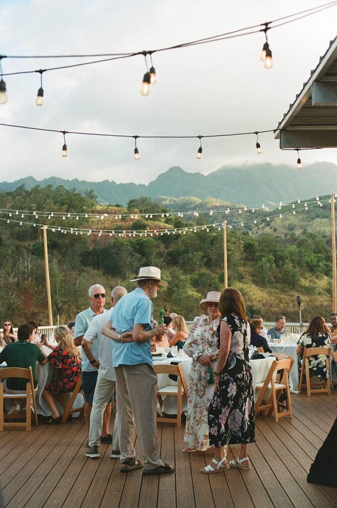 Guests mingling under string lights during an outdoor reception at one of the most picturesque Wedding Venues in Hawaii, surrounded by lush mountains.
