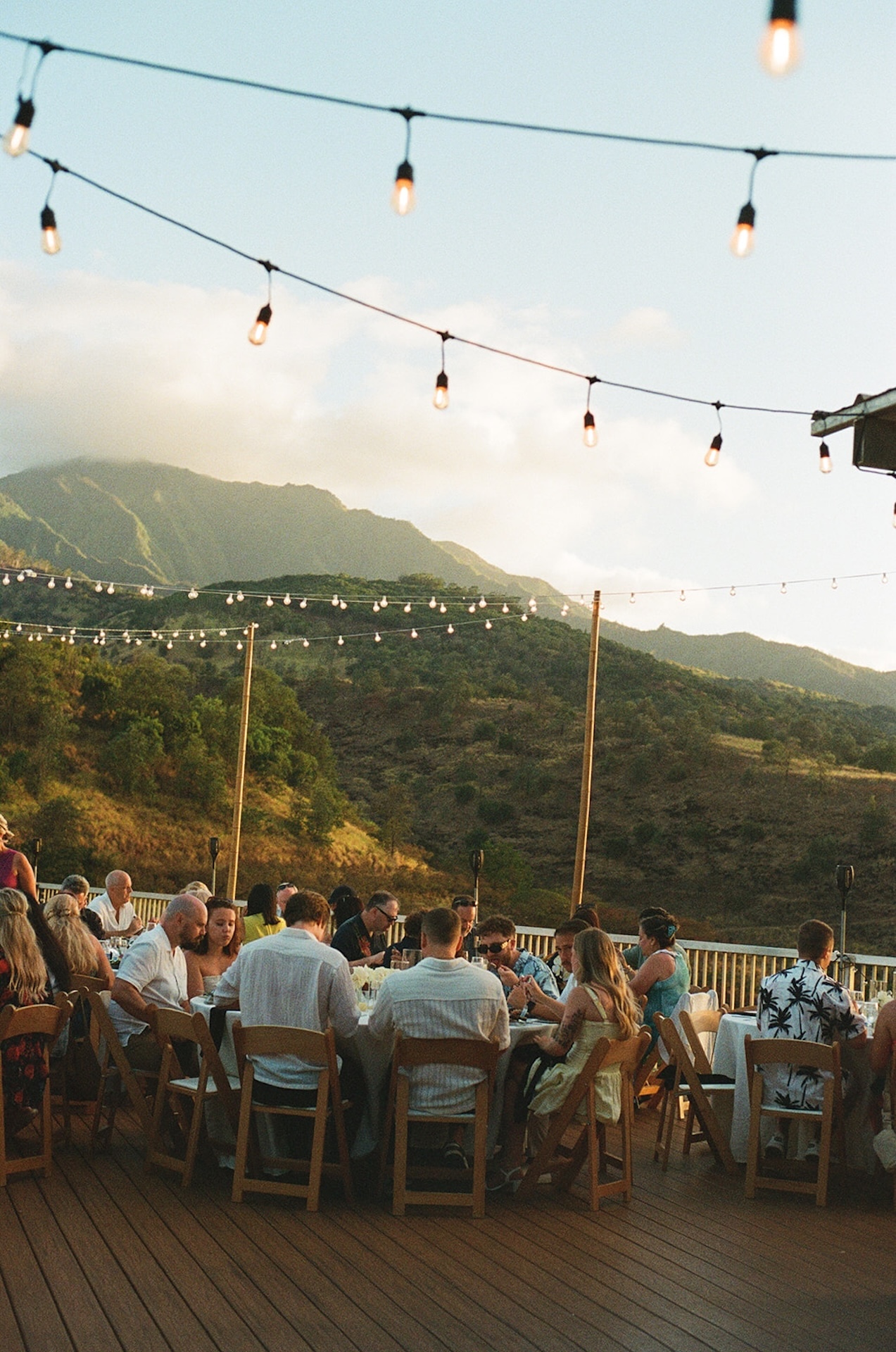 Guests mingling and laughing under the glow of bistro lights as the sun sets over the mountains.