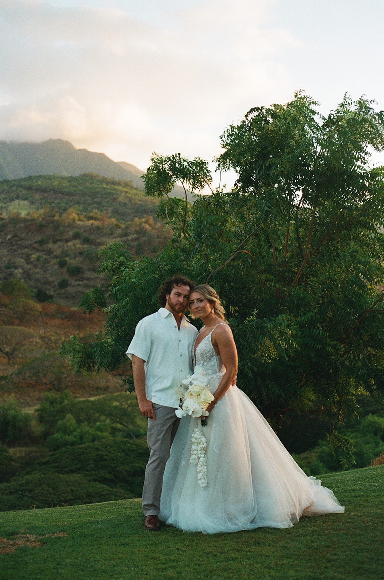 Bride and groom posing together under a tree with soft evening light and lush greenery surrounding them — a romantic moment at one of the best Wedding Venues in Hawaii.